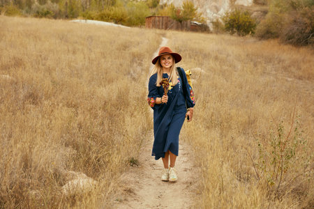 Female Traveler With Flowers In Hand At Autumn Field, Stylish Girl Traveling In Nature. High...