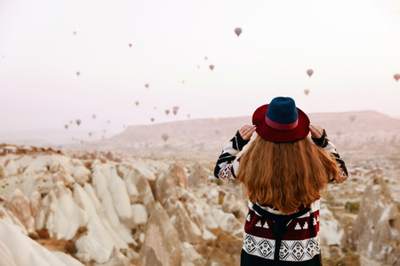 Travel. Beautiful Woman In Hat Watching Flying Hot Air Balloons From Hill. Female In Ethnic Clothes In Cappadocia. High Resolutionの写真素材