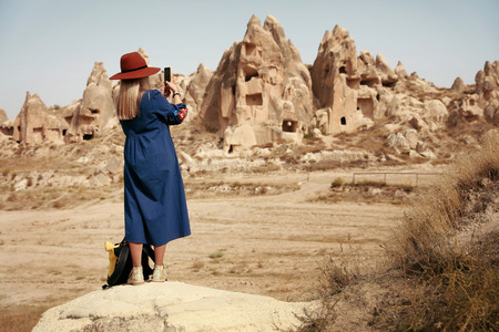 Woman Traveling And Taking Photos Of Landscape On Phone. Female In Hat Photographing Caves In Rocks. High Resolutionの写真素材