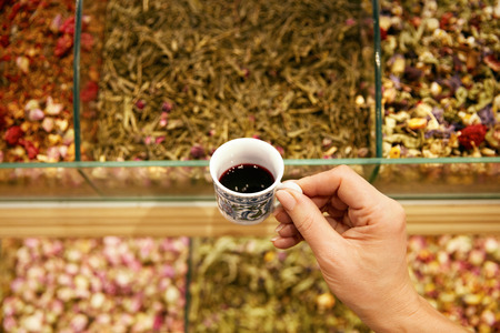 Hand With Cup Of Turkish Red Tea In Store Closeup, Assortment Of Tea On Background At Market. High Resolutionの写真素材
