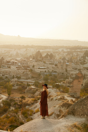 Travel. Woman In Dress Standing On Hill With Turkish Town On Background, Female Traveler At Cappadocia Turkey. High Resolutionの写真素材