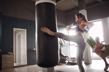 Sports woman doing kickboxing training, kicking heavy boxing bag with leg at sport club. Female athlete doing fighting workoutの写真素材