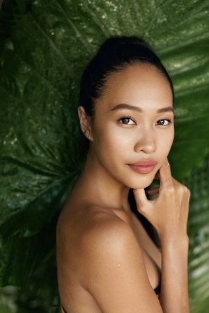 Beauty face. Woman model with natural makeup and healthy skin in tropical nature. Beautiful asian girl portrait with jungle leaves on backgroundの写真素材
