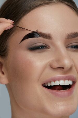 Eyebrow cosmetics. Woman taking off brow gel tint from eyebrow closeup. Girl model peeling off peel-off eyebrow beauty productの写真素材
