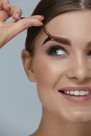 Eyebrow cosmetics. Woman taking off brow gel tint from eyebrow closeup. Girl model peeling off peel-off eyebrow beauty productの写真素材