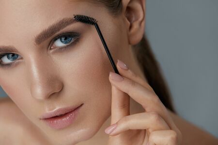 Eyebrow makeup. Woman brushing brows with brush closeup. Girl model with beautiful eyes shaping eyebrows with brow gelの写真素材