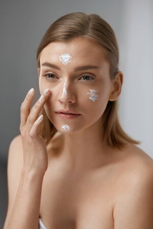 Skin care. Woman applying facial cream on beauty face closeup. Girl model with natural makeup using moisturizing cosmeticsの写真素材