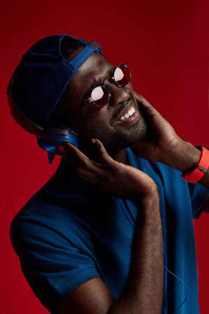 Listen music. Smiling black man in headphones listening sounds portrait on red background. Happy...