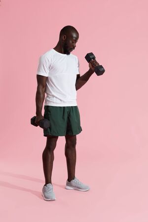 Exercise. Sports man doing dumbbell biceps workout on colorful background. Fitness male model in stylish active wear exercising, doing dumbbell curlの写真素材