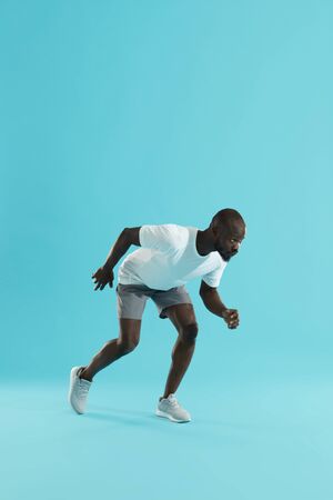 Sport. Man runner standing in running start pose on blue color background. Sporty male athlete in stylish sports wear preparing to run at studioの写真素材