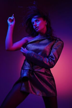 Fashion woman model in fashionable dress in colorful neon lights at studio. Portrait of stylish sexy girl in trendy clothes over bright pink and purple ultraviolet light at night club. Styleの写真素材