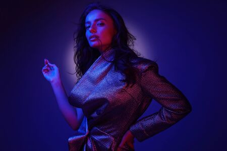 High fashion girl model in stylish clothing in colorful neon lights. Studio portrait of beautiful sexy woman in glamour dress over pink and purple ultraviolet background at night clubの写真素材