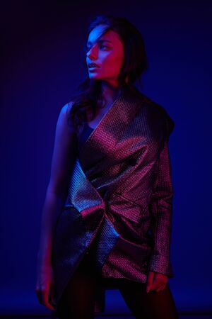 Women style. Fashion model in stylish dress in colorful neon lights at studio portrait. Fashionable sexy girl in glamorous clothes in pink and purple ultraviolet colors at night clubの写真素材