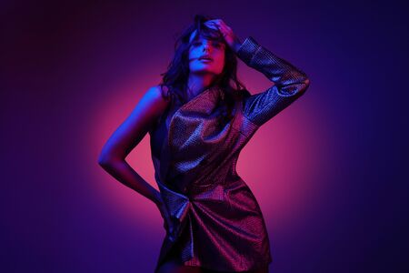 Fashion model in stylish clothing on colorful neon lights in studio. Portrait of beautiful sexy girl in trendy clothes over bright vivid pink and purple ultraviolet background at night club. Styleの写真素材