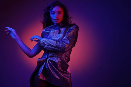 Fashion model in stylish clothing on colorful neon lights in studio. Portrait of beautiful sexy girl in trendy clothes over bright vivid pink and purple ultraviolet background at night club. Styleの写真素材