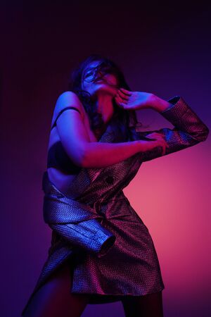 Fashion woman model in fashionable dress in colorful neon lights at studio. Portrait of stylish sexy girl in trendy clothes over bright pink and purple ultraviolet light at night club. Styleの写真素材