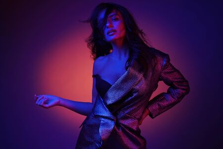 Fashion model in stylish clothing on colorful neon lights in studio. Portrait of beautiful sexy girl in trendy clothes over bright vivid pink and purple ultraviolet background at night club. Styleの写真素材