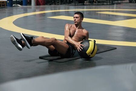 Man doing fitness workout, practicing abs exercise with med ball at street. Male athlete exercising, doing russian twist with medicine ball outdoorsの写真素材