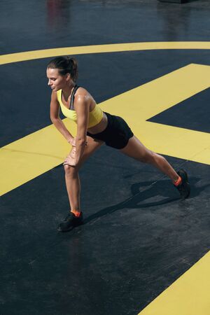 Fitness woman in sportswear stretching legs before workout outdoors. Full length portrait of fit girl in sport clothes warming up at streetの写真素材