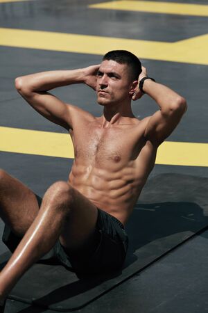 Sport man doing abs crunches exercise, fitness workout at street. Male athlete exercising on yoga mat, doing abdomen muscle training outdoors at gymの写真素材
