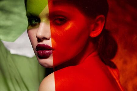 Fashion makeup. Woman model with beauty face and red lips in colorful light. Portrait of girl with glamour make-up, trendy lipstick and glowing skin under bright green and red neon color at studioの写真素材