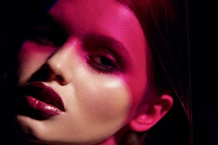 Makeup beauty. Woman model with dark lipstick under pink light. Closeup portrait of glamorous girl with beautiful sexy make-up, lip gloss and glowing skin under color lights. High quality imageの写真素材
