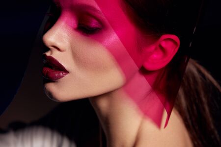 Makeup beauty. Woman model with dark lipstick under pink light. Closeup portrait of glamorous girl with beautiful sexy make-up, lip gloss and glowing skin under color lights. High quality imageの写真素材