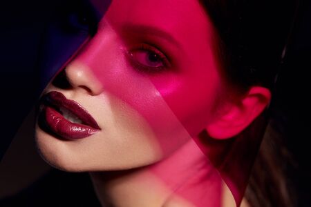 Makeup beauty. Woman model with dark lipstick under pink light. Closeup portrait of glamorous girl with beautiful sexy make-up, lip gloss and glowing skin under color lights. High quality imageの写真素材