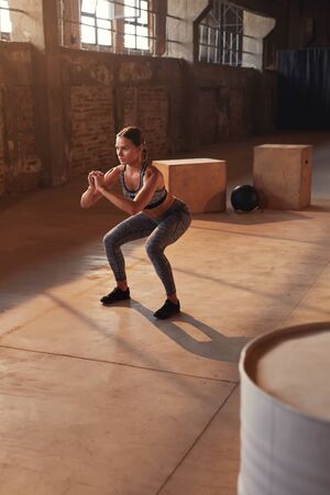 Fitness workout. Sport woman doing squat leg exercise at gym. Beautiful girl athlete with fit body in sportswear exercising, having functional training indoorsの写真素材