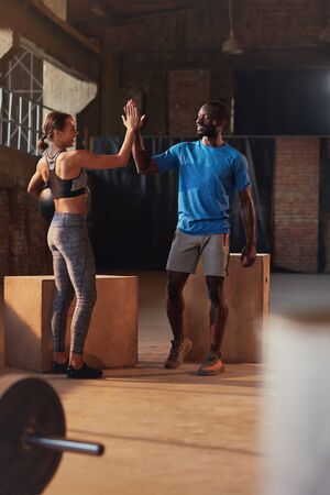 Sport couple giving high five after fitness workout at gym. Happy smiling people celebrating successful functional training competition indoorsの写真素材