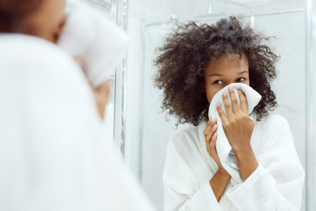 Washing face. Closeup of woman drying skin with towel looking in mirror at bathroom. Portrait of...