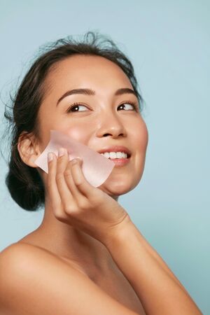 Face skin care. Smiling woman using oil blotting paper portraitの写真素材
