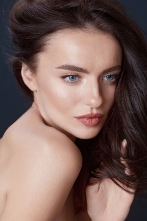 Beautiful Girl. Woman Touching Hair Close Up Portrait. Blue-Eyed Brunette With Smooth Perfect Skin And Natural Makeup On Black Background. Young Model Looking Away.の写真素材