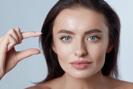 Beauty Face. Young Woman Close Up Portrait. Beautiful Model Holding Something In Hand. Brunette With Perfect Skin, Blue Eyes And Natural Makeup Looking At Camera.の写真素材