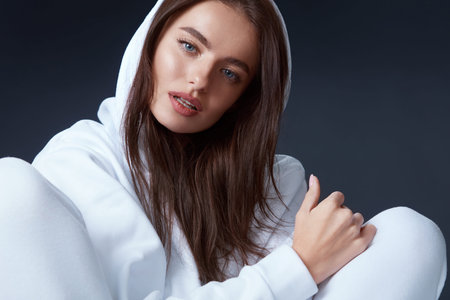 Stylish Girl. Beautiful Model In Hoodie Portrait. Sensual Brunette In White Casual Clothes Sitting...