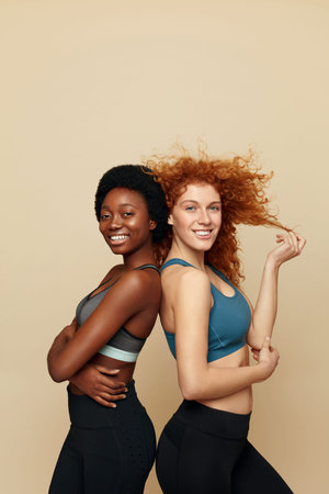 Fitness Women. Beautiful Ethnic Girls Portrait. Sporty African Brunette And Caucasian Redhead Posing On Beige Background. Sport As Lifestyle. の写真素材