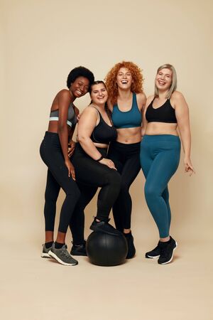 Diversity Models. Different Race And Size Women. Group Of Multicultural Friends In Sportswear With Black Fitness Ball On Beige Background. Sport For Active Lifestyle.の写真素材