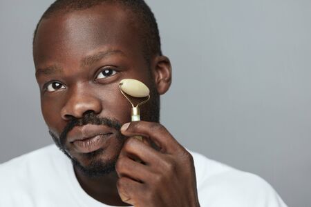 Facial Beauty Routine. Jade Roller Face Massage For African Man. Anti Aging Skincare Treatment.の写真素材