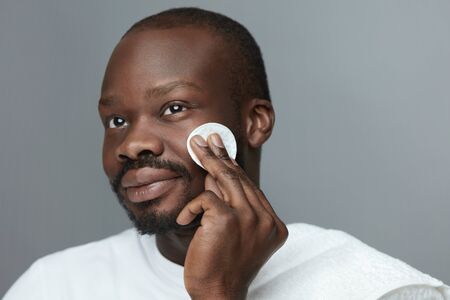 Face Skincare. Male African Model Cleans Facial Skin With Round Cotton Pad. Beauty Treatment Routine For Man.の写真素材