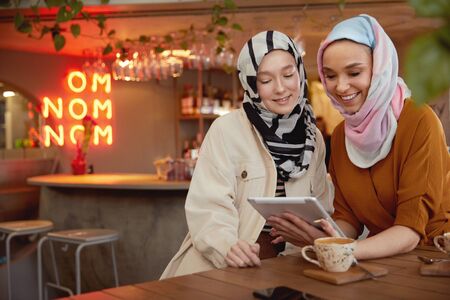 Women. Young Girls In Hijab. Friends Meeting In Cafe. Smiling Muslim Female Drinking Coffee And Looking On Tablet.の写真素材