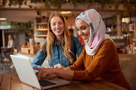 Business. Colleagues Meeting In Cafe. Diversity Ethnic Women. Smiling Girl In Hijab Working On Laptop, Blonde Looking At Screen.の写真素材