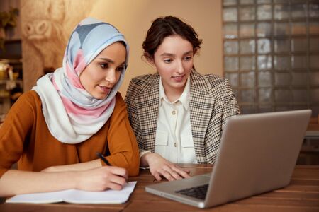 Business. Women Meeting In Cafe. Diversity Ethnic Colleagues Working On Laptop. Girl In Hijab Writing, Brunette Showing Something At Screen.の写真素材