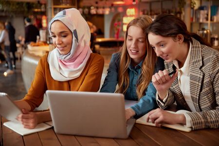 Friends. Women Meeting In Cafe. Three Young Girls With Laptop And Tablet Working At Bistro. Diversity Colleagues Spending Time In Restaurant. Freelance As Lifestyle.の写真素材