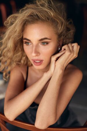 Beautiful Woman. Sexy Blonde Model Relaxing On Wooden Chair. Healthy Natural Look In Beauty Portrait. Female Curly Hairstyle And Nude Makeup.の写真素材