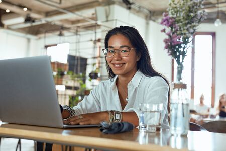 Freelancer. Business Woman Working On Laptop Remotely At Cafe. Fashion Girl In Glasses Sitting In Restaurant And Typing Something. Smiling Female Looking At Camera Portrait.の写真素材