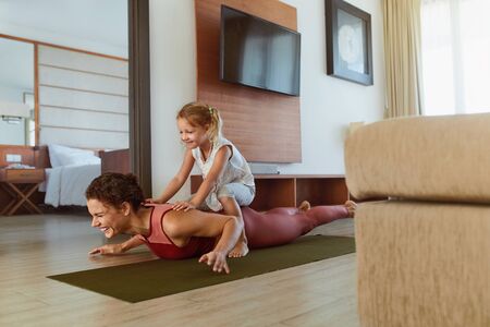 Workout. Parent And Child Exercising Together At Home. Happy Woman And Daughter Having Fun In Living Room. Little Girl Sitting On Sporty Motherâs Back And Laughing. の写真素材