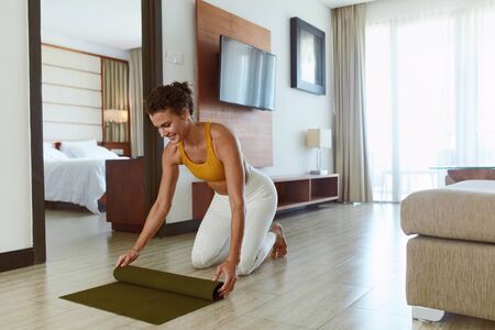 Home Workout. Woman Rolling Yoga Mat After Exercising. Female In Sportswear Folding Fitness Rug After Completing Daily Sport Routine. Staying Active And Fit During Social Isolation.の写真素材