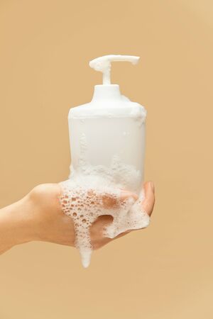 Personal Hygiene. Hand Covered With Foam Holding Liquid Soap Bottle On Beige Background. Washing Hands For COVID-19 Prevention And Staying Healthy.の写真素材