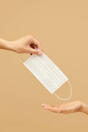 Protection. Hands With Face Mask For COVID-19 Infection Prevention. Female Giving White Surgical Mask To Somebody On Beige Background. Using Medical Equipment For Healthcare.の写真素材