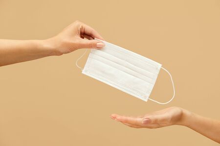 Surgical Mask. Hand Giving Medical Coronavirus Protective Mask On Beige Background. Wearing Personal Protection Clothes For Virus And Bacterial Infection Prevention.の写真素材